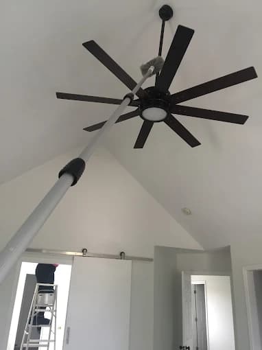 Professional cleaning team using an extended pole duster to clean a high ceiling fan in a vaulted-ceiling home