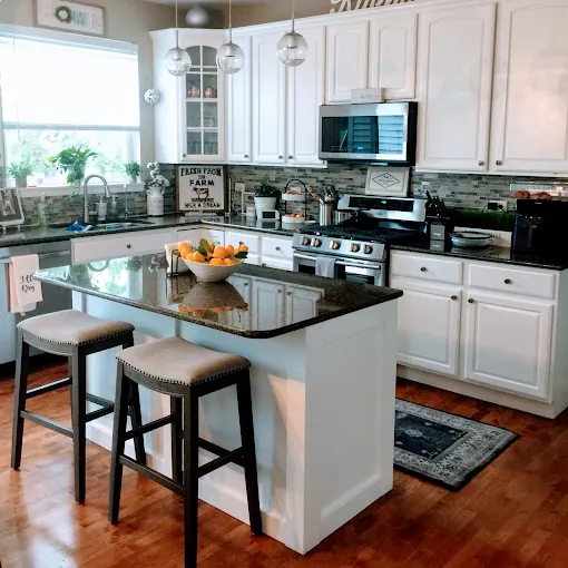 An ordered, sparkling kitchen with white cabinets and a clean island countertop, cleaned by Wonderful Laura Cleaning in Aurora, IL