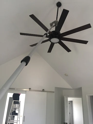 Professional cleaning team using an extended pole duster to clean a high ceiling fan in a vaulted-ceiling home